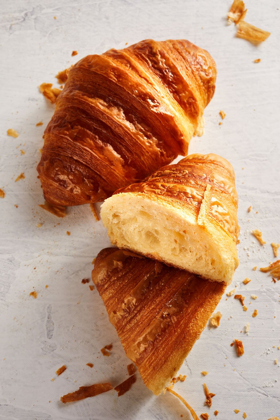 Two croissants, one cut in half to show fluffy inside