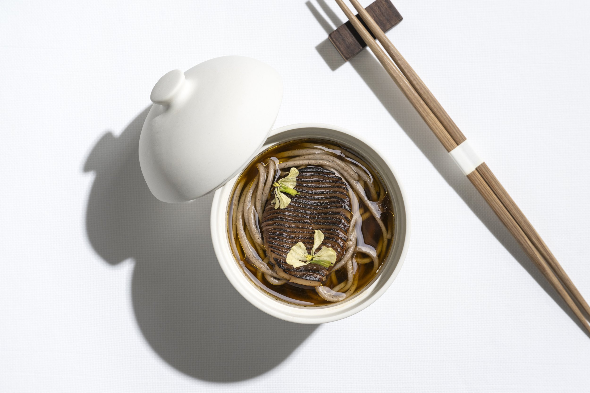 Bowl of soba noodles and a pair of chopsticks on a white tablecloth.