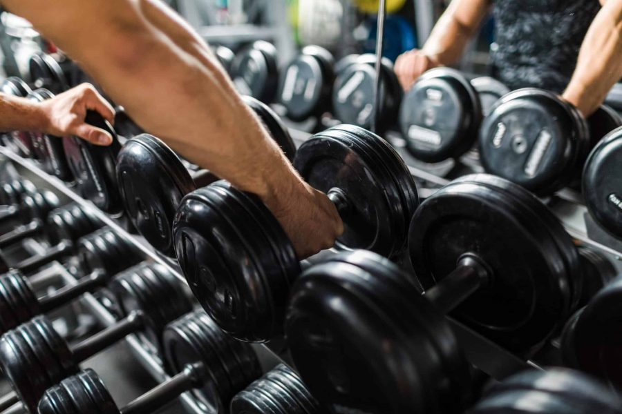 Closeup shot of muscular male arm picking up heavy weights from dumbbell rack in modern gym