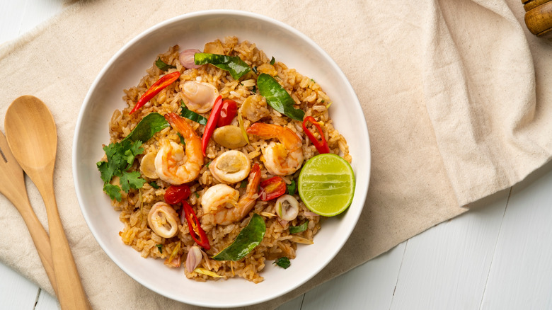 stir fry with seafood in a white bowl with wooden spoon and fork