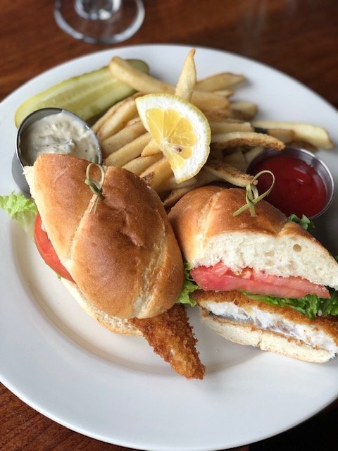 Fridays Fried haddock sandwhich with lettuce tomato on a long roll with Fries and a side of tartar sauce